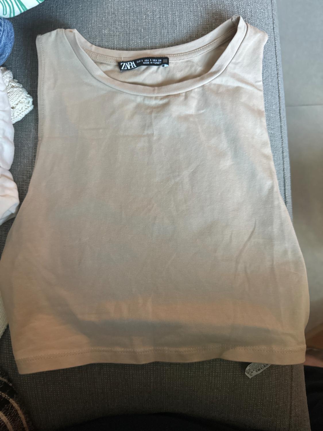 Front view of a beige sleeveless t-shirt on a grey surface.