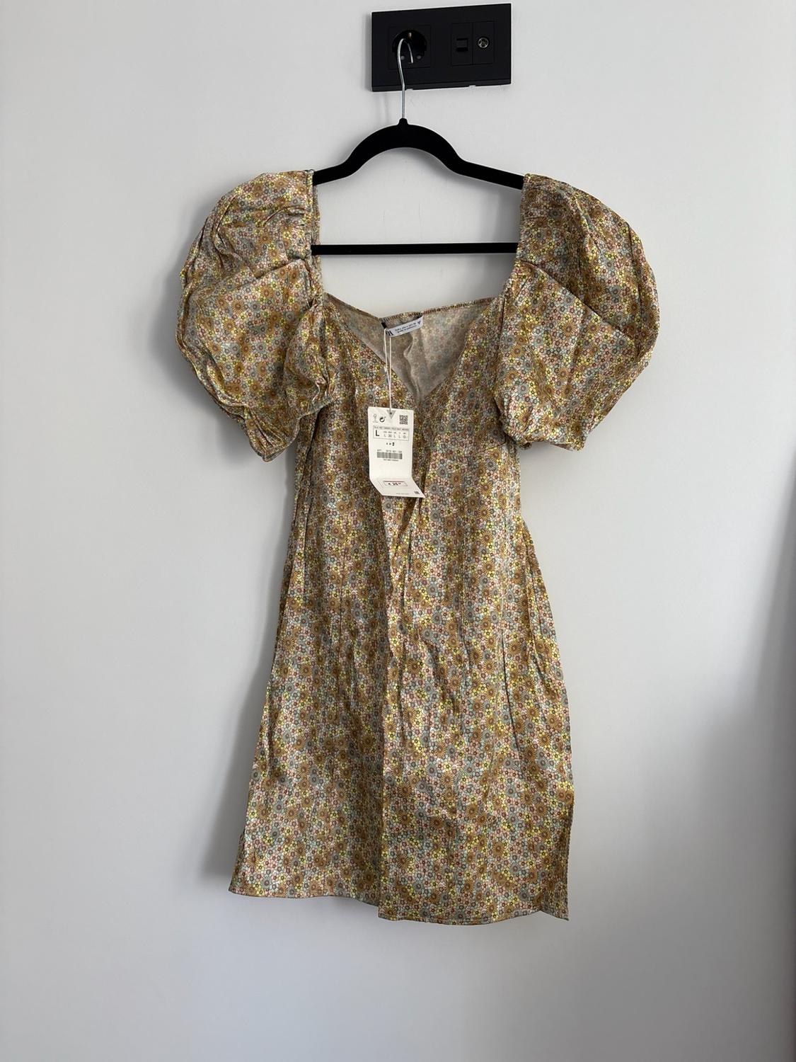 Short floral print dress with puff sleeves and a V-neckline, hanging on a black hanger against a white wall.