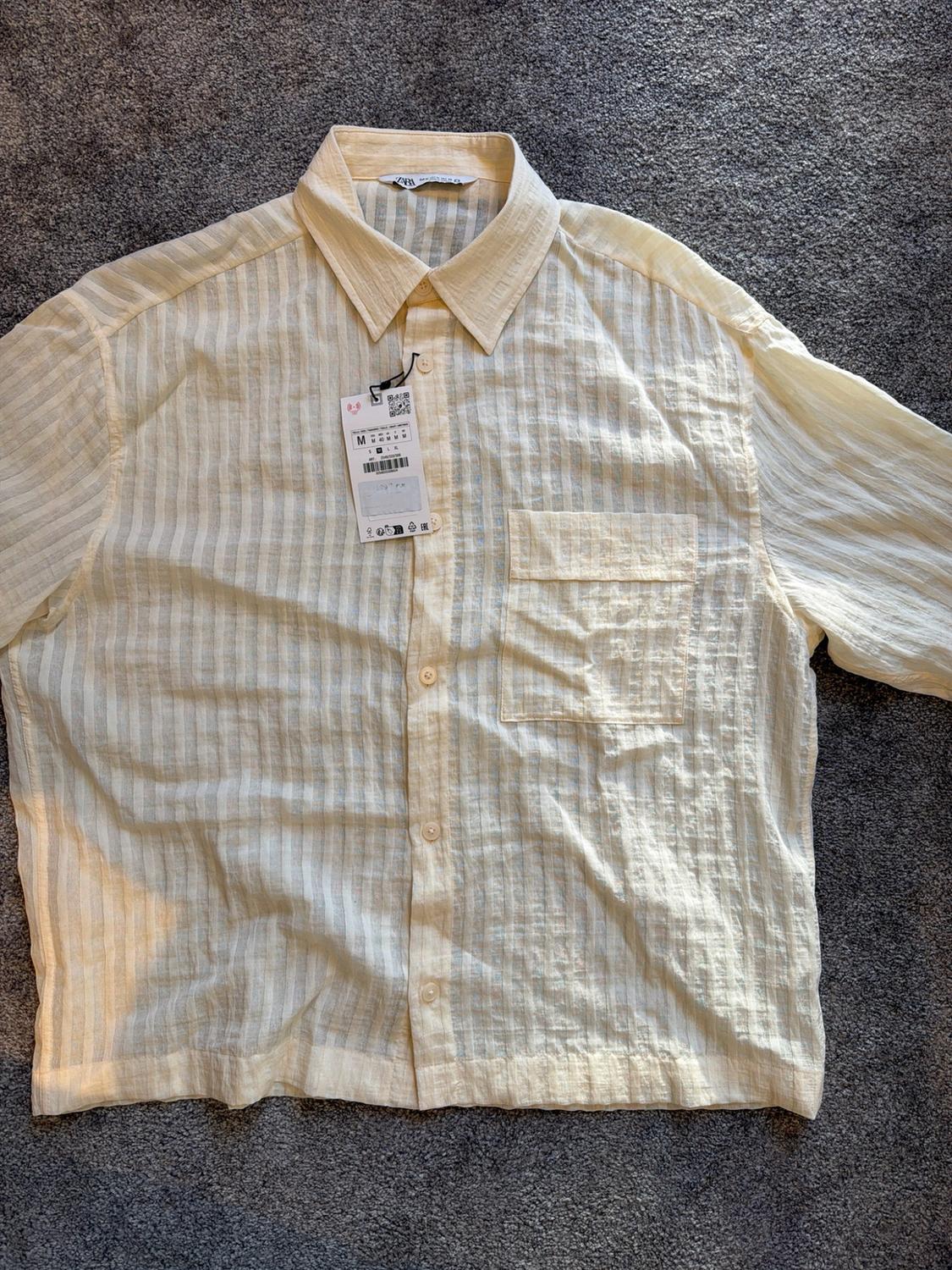 Light yellow button-down shirt with vertical stripes and a chest pocket, on a grey background. Label text: ZARA M.