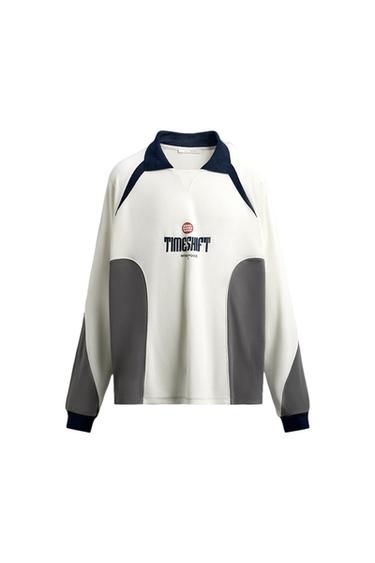 White sweatshirt with grey details and a navy blue collar. "TIMESHIFT INTERFOCUS" text on the front with a small red logo.