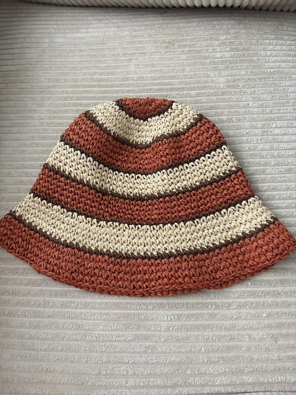 Knitted bucket hat with terracotta, beige and dark brown stripes, on a light fabric surface.