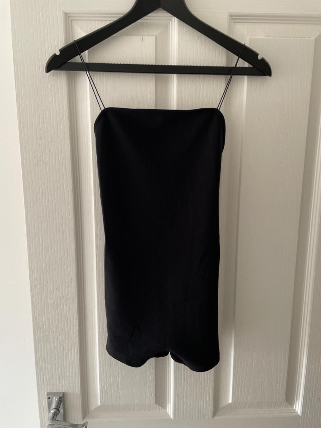 Short black dress with spaghetti straps hanging on a black hanger over a white panelled door. Minimalist style.