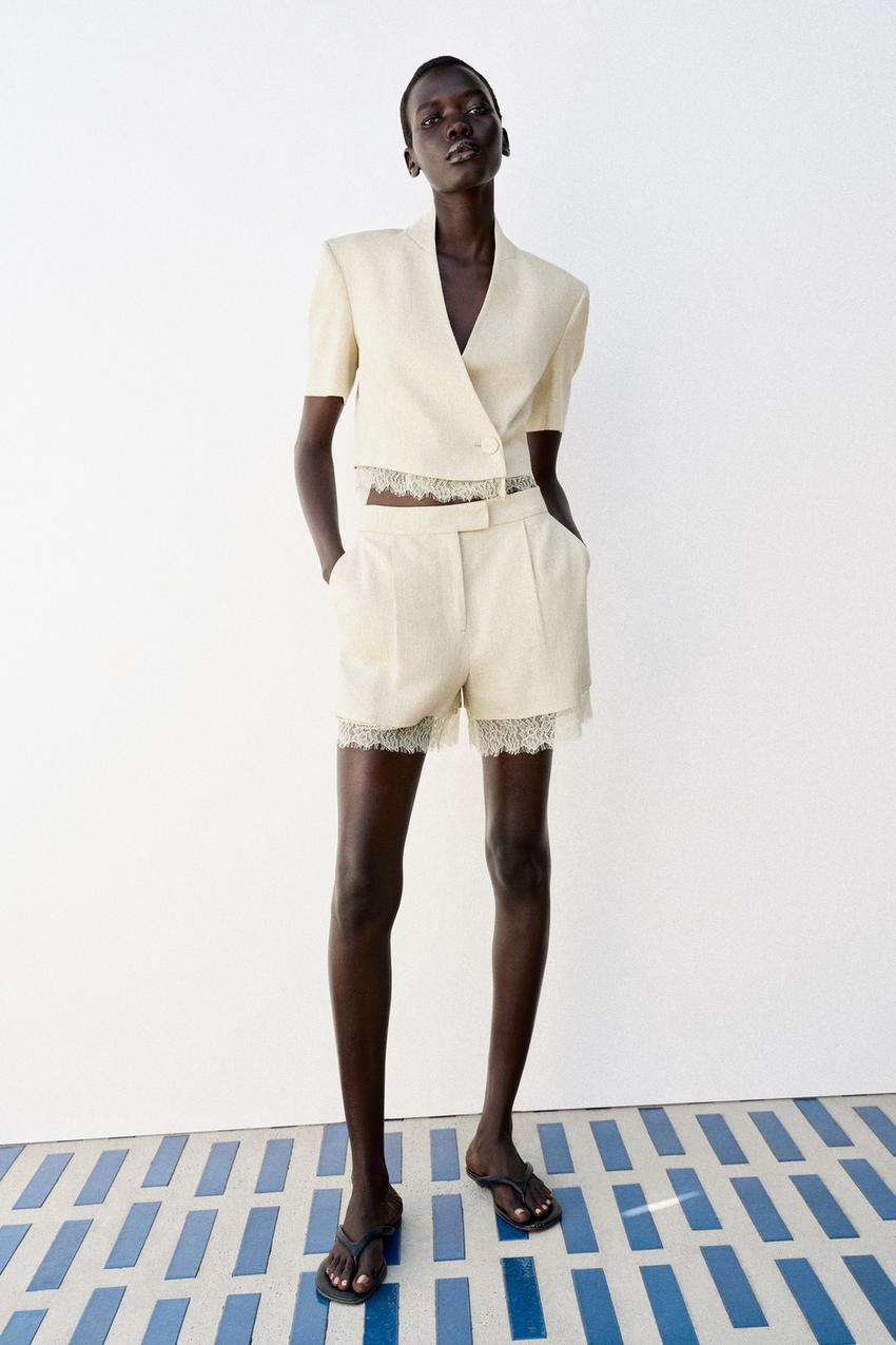 Beige short-sleeved jacket set, double-breasted with one button, and pleated shorts with side pockets, both with lace hems.