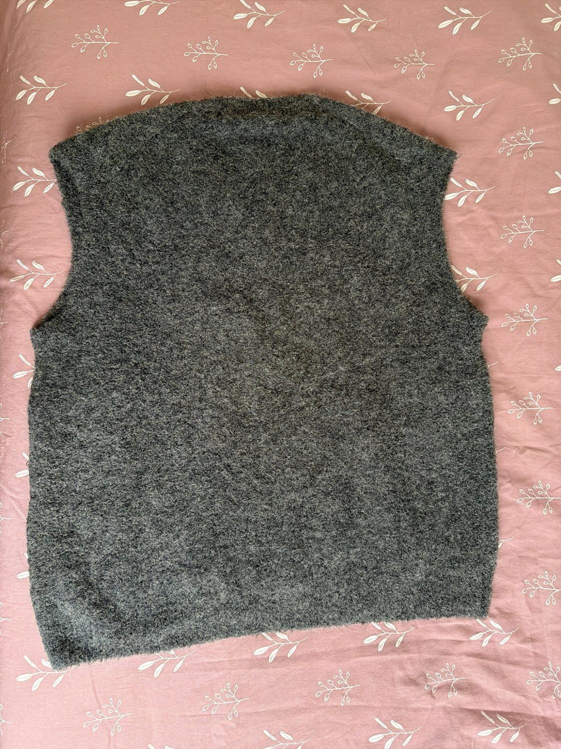 Dark gray sleeveless knit vest with a soft texture, over a pink fabric background with a white leaf print.