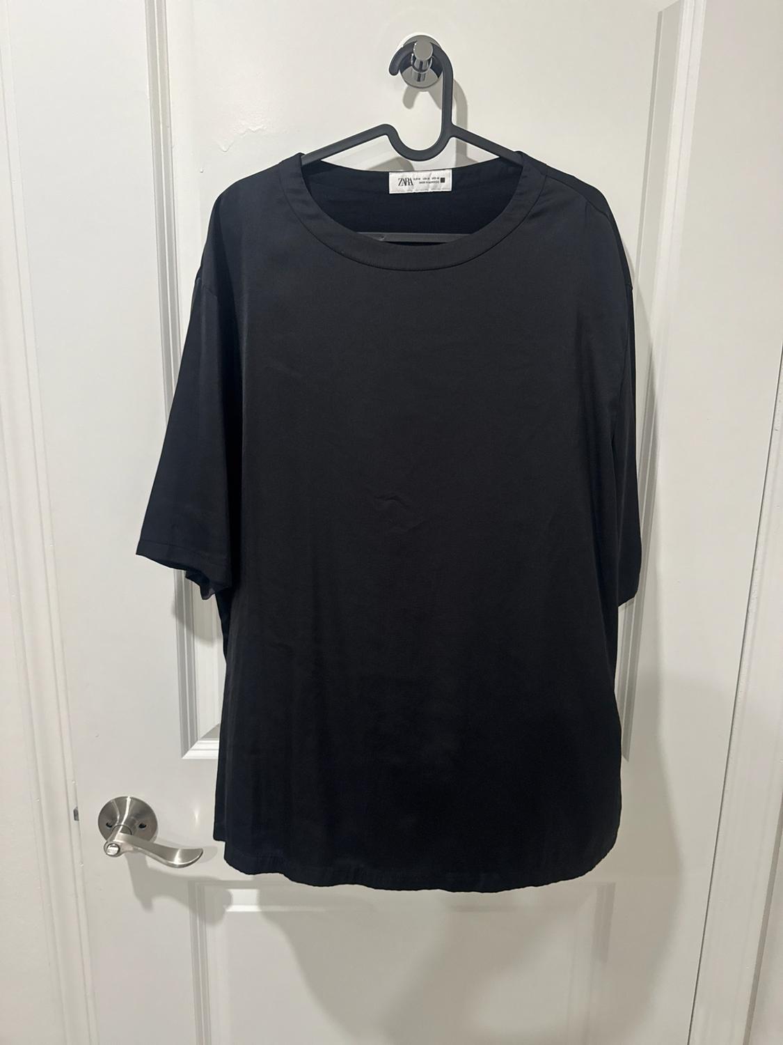 Black short-sleeve T-shirt hanging on a hanger over a white door. The label reads ZARA.