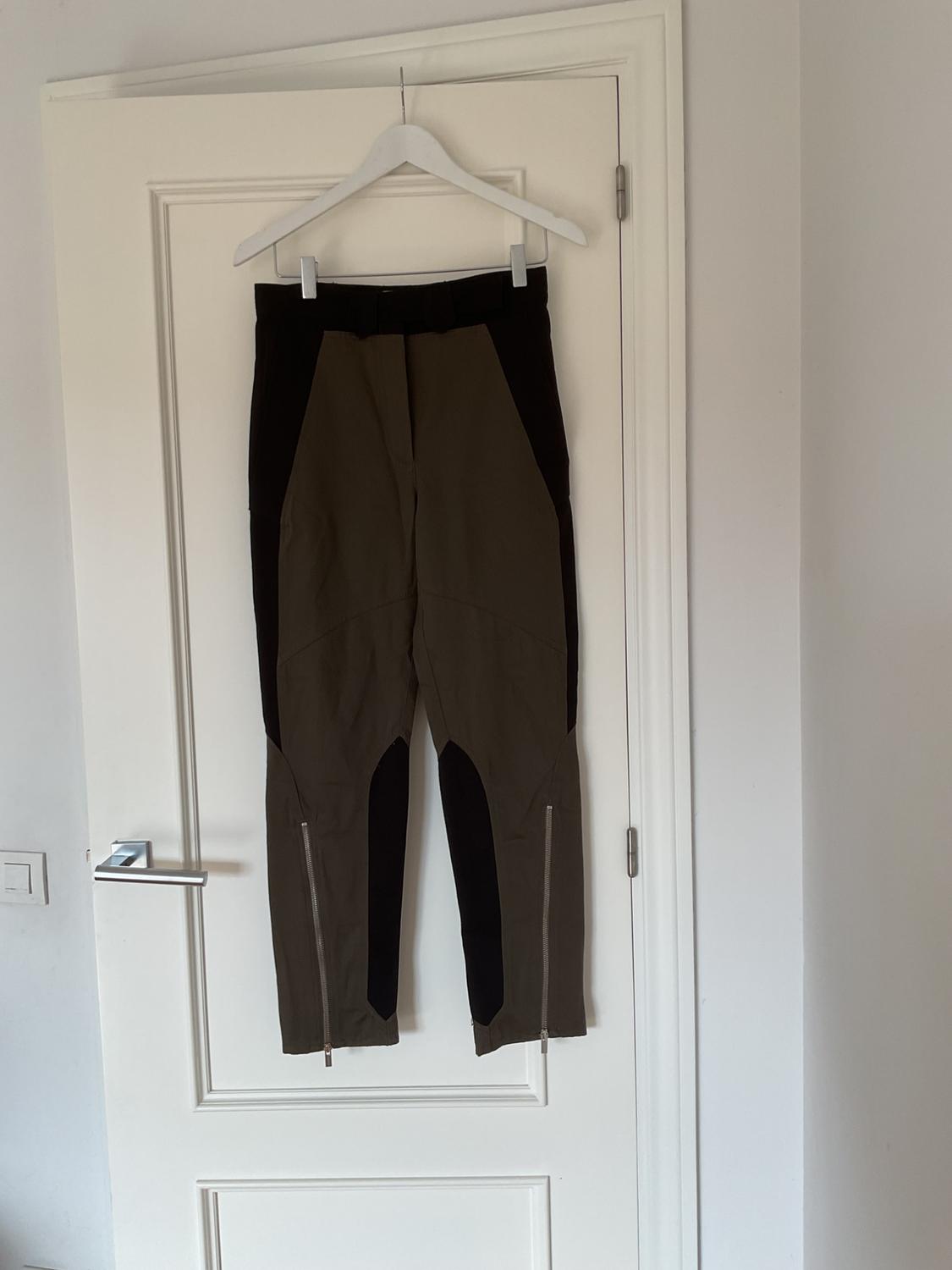 Trousers hanging on a white hanger over a white door. Two-tone design with ankle zips.