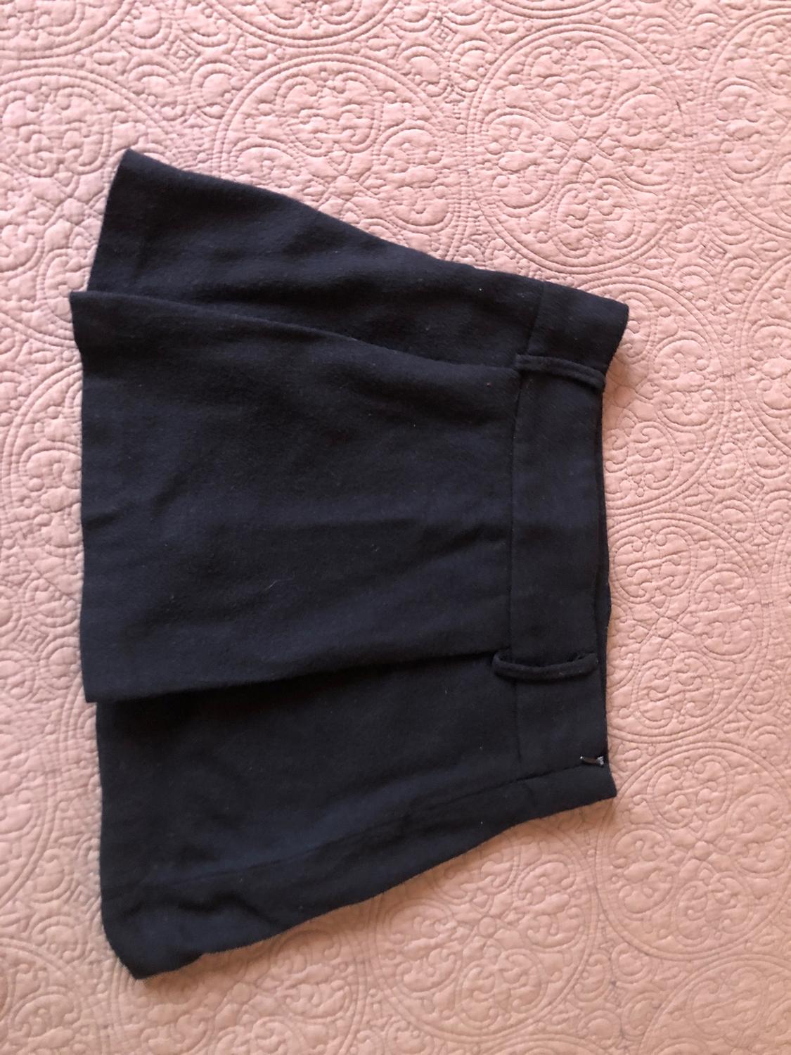 Black mini skirt on a pink bedspread with a circular pattern design. The skirt's fabric appears soft and lightweight.
