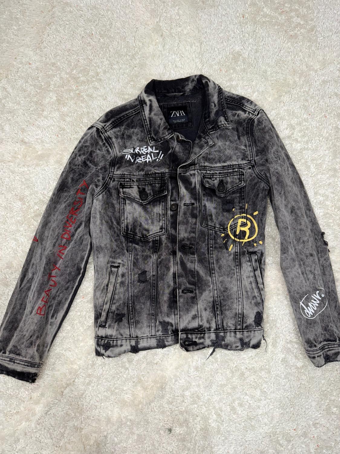 Grey denim jacket on a white rug with the texts: ZARA, SURREAL IN REAL!!, BEAUTY IN DIVERSITY, dwnr. and a yellow logo.