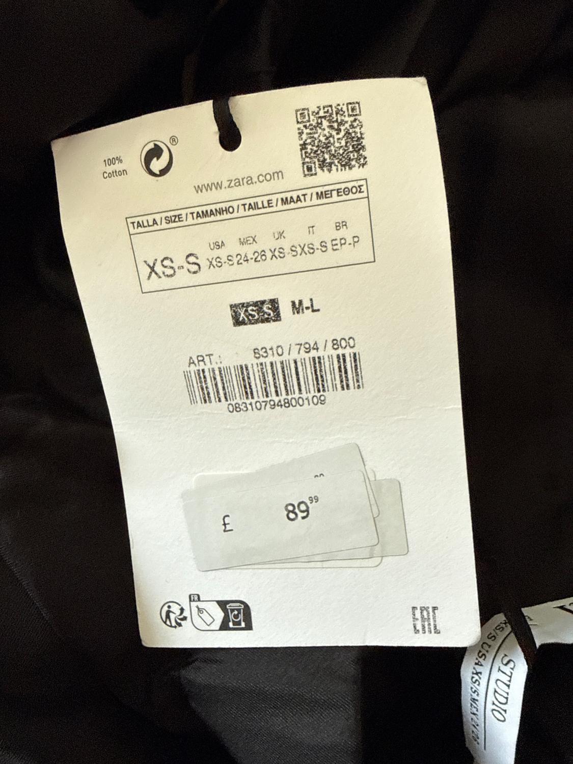 Zara clothing label with sizes XS-S and M-L, price £89.99, barcode and QR. Black fabric background.
