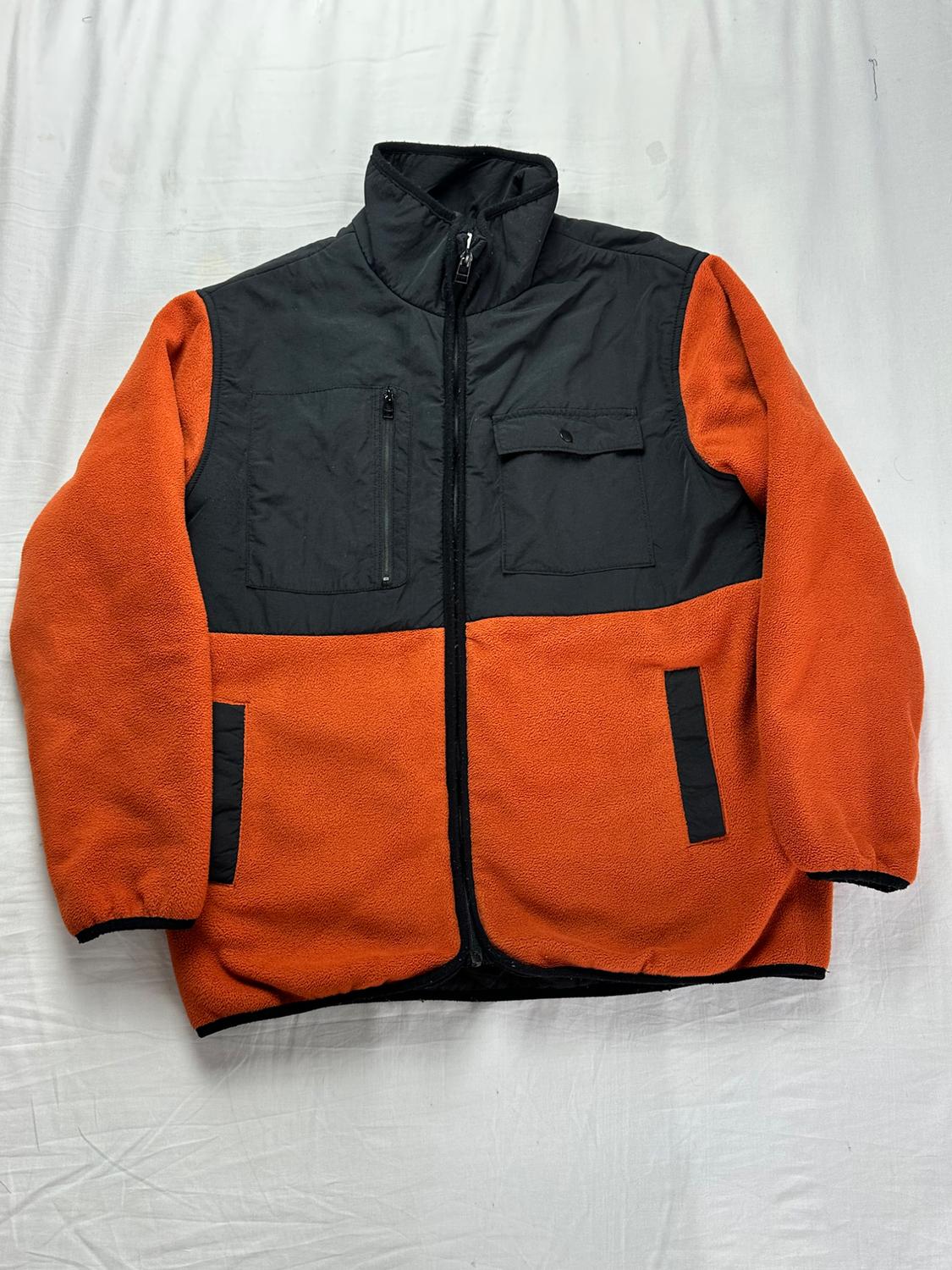 Naranja fleece-lined jacket with black panels on the chest, high collar, front zipper, and side pockets on a white background.