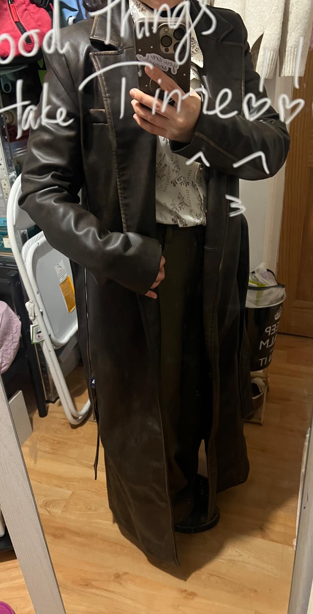Person in a long brown coat and patterned shirt takes a photo in the mirror. Text in the mirror: "Good things take time".