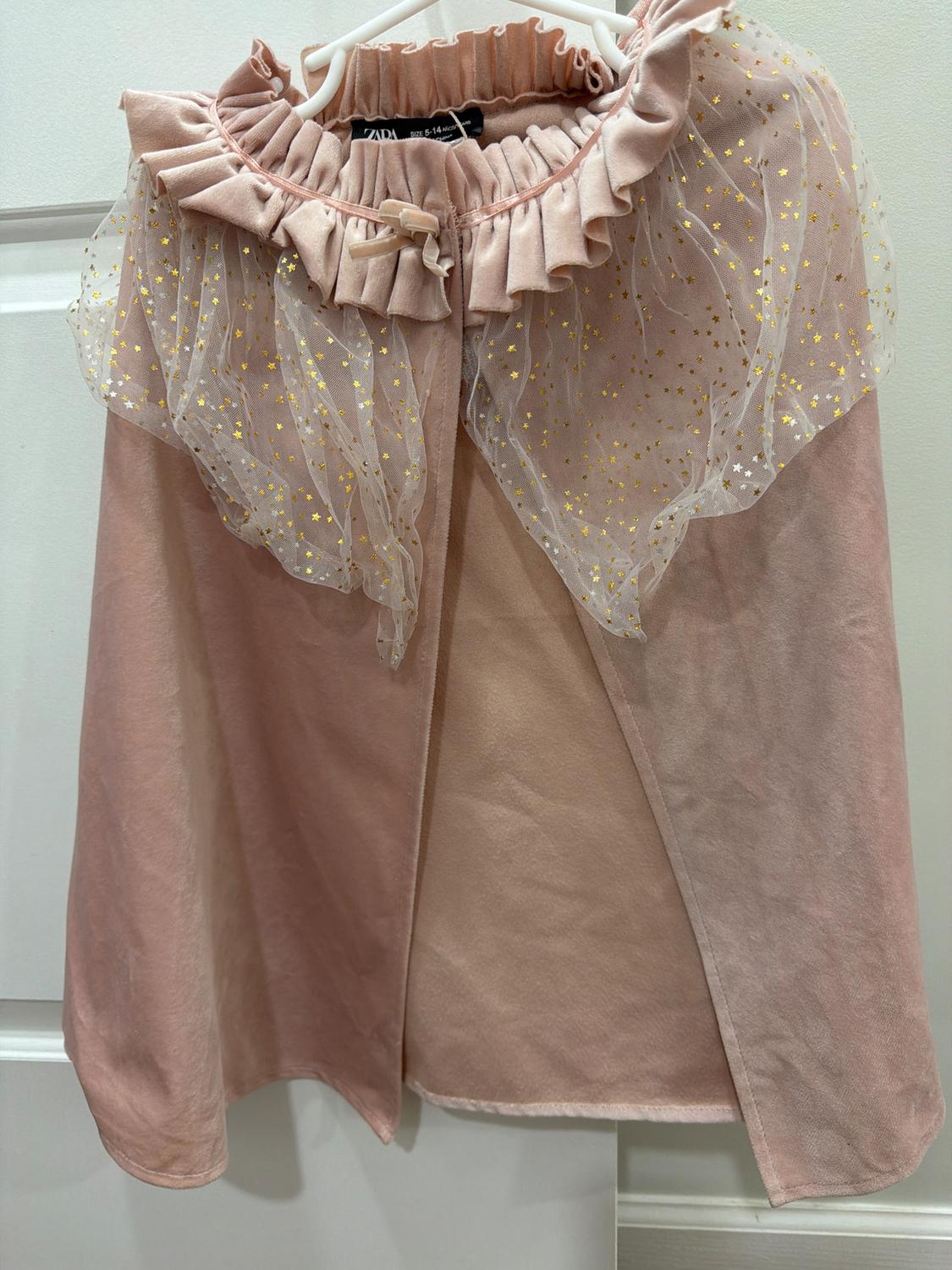 Pink cape with ruffles and sheer tulle with gold stars, hanging on a white hanger.