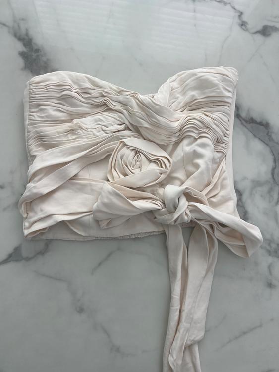 White draped top with knot and pleat detail, on a light gray marble background.