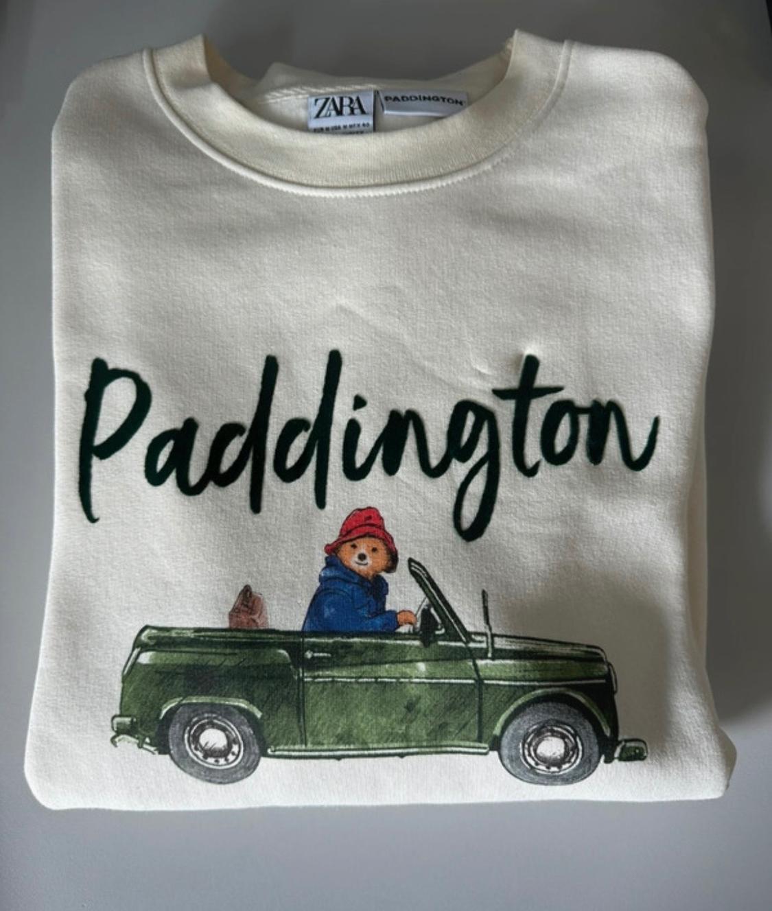 White sweatshirt with "Paddington" print and a drawing of a bear in a green car. Visible Zara tag.
