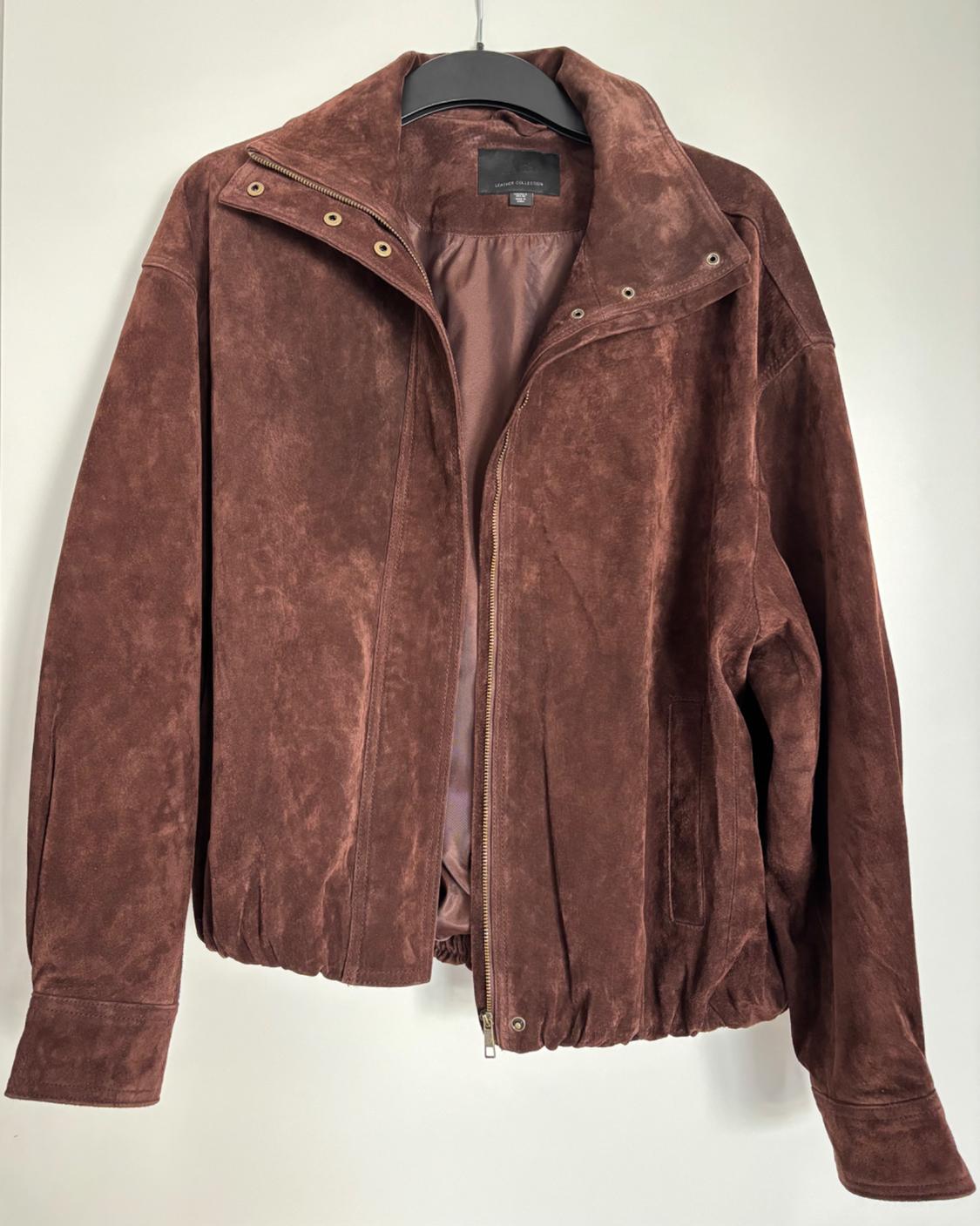 Brown suede jacket hanging on a black hanger, with a front zip and gold buttons at the neck. White background.