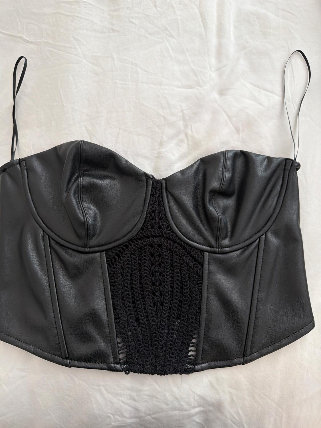 Black camisole with corset design and lace detail in the center, on a wrinkled white background.