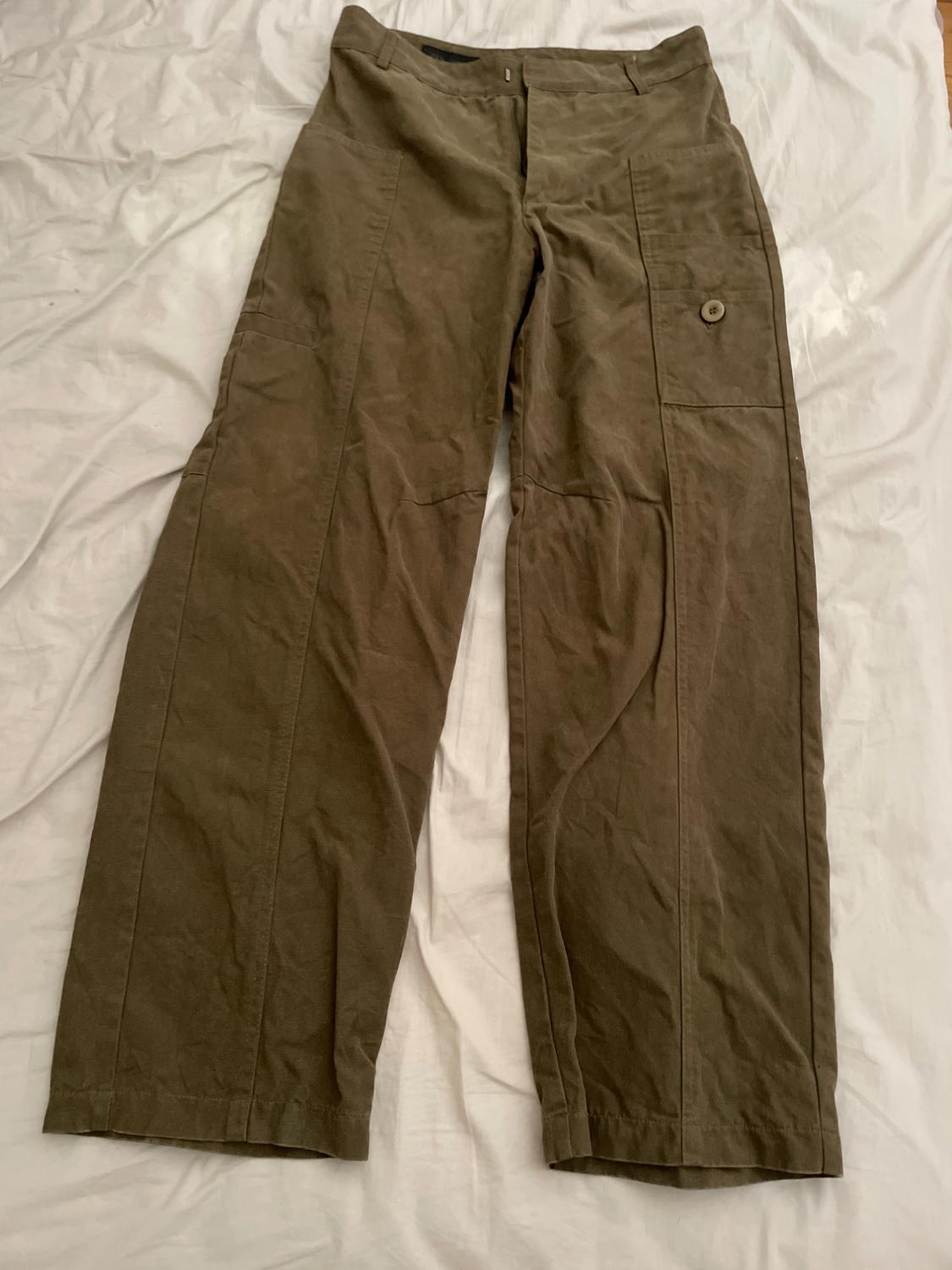 Brown wide-leg trousers with a side pocket and button, placed on a wrinkled white sheet.