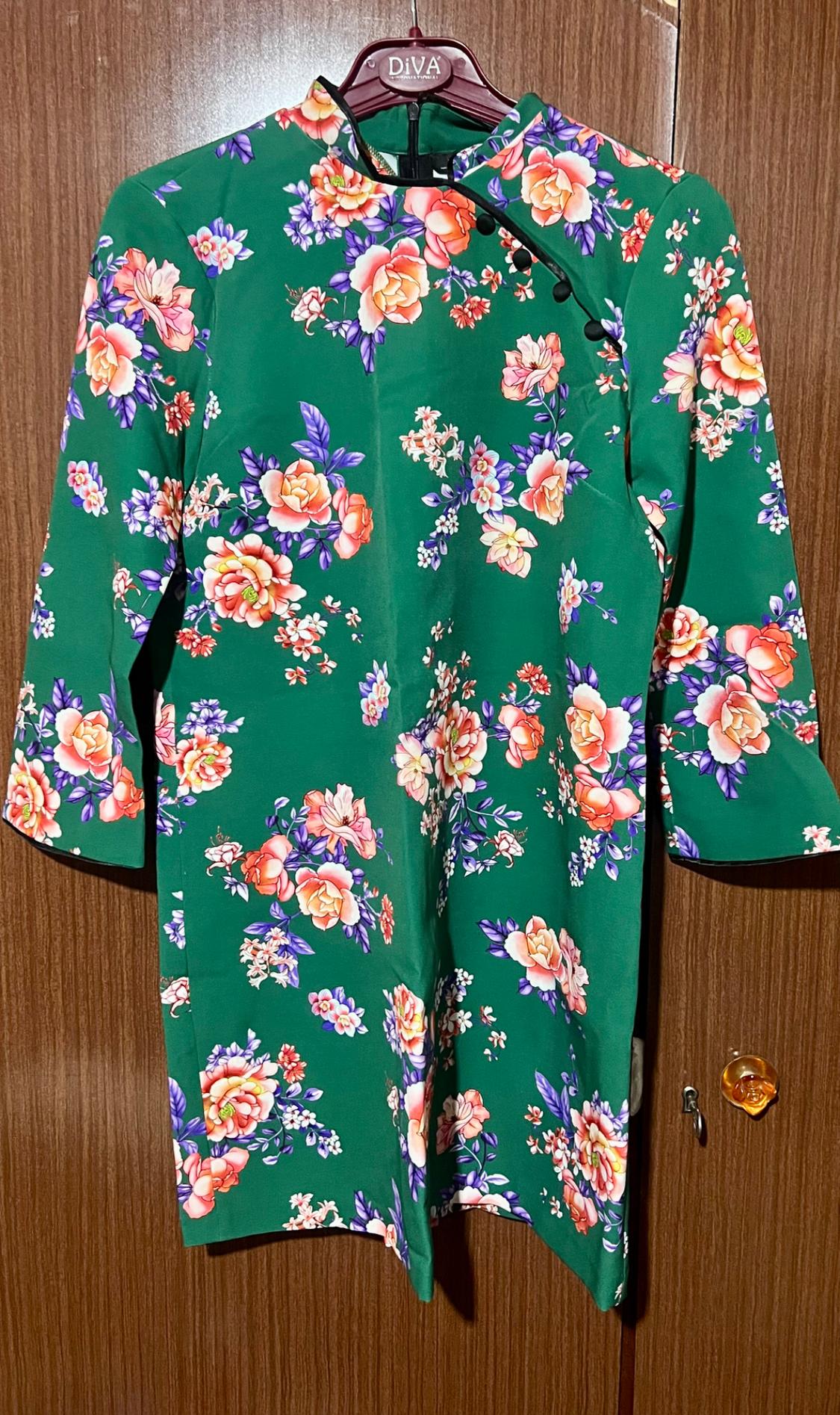 Green dress with a floral print in pink and purple tones, hanging on a brown hanger with the brand "DiVA".