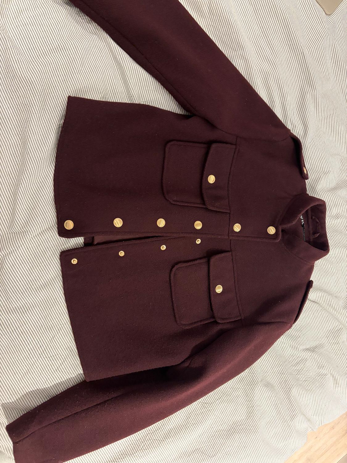 Burgundy jacket with gold buttons and large pockets on a white and grey striped fabric surface.