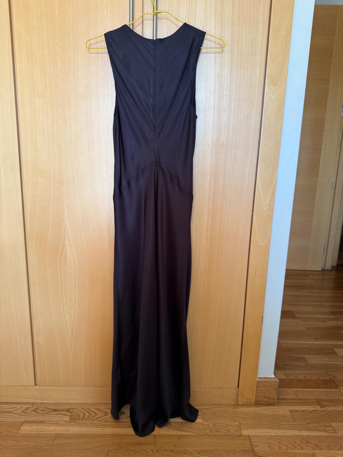Black long dress hanging on a yellow hanger over a light wood door. The design is sleeveless and straight cut.