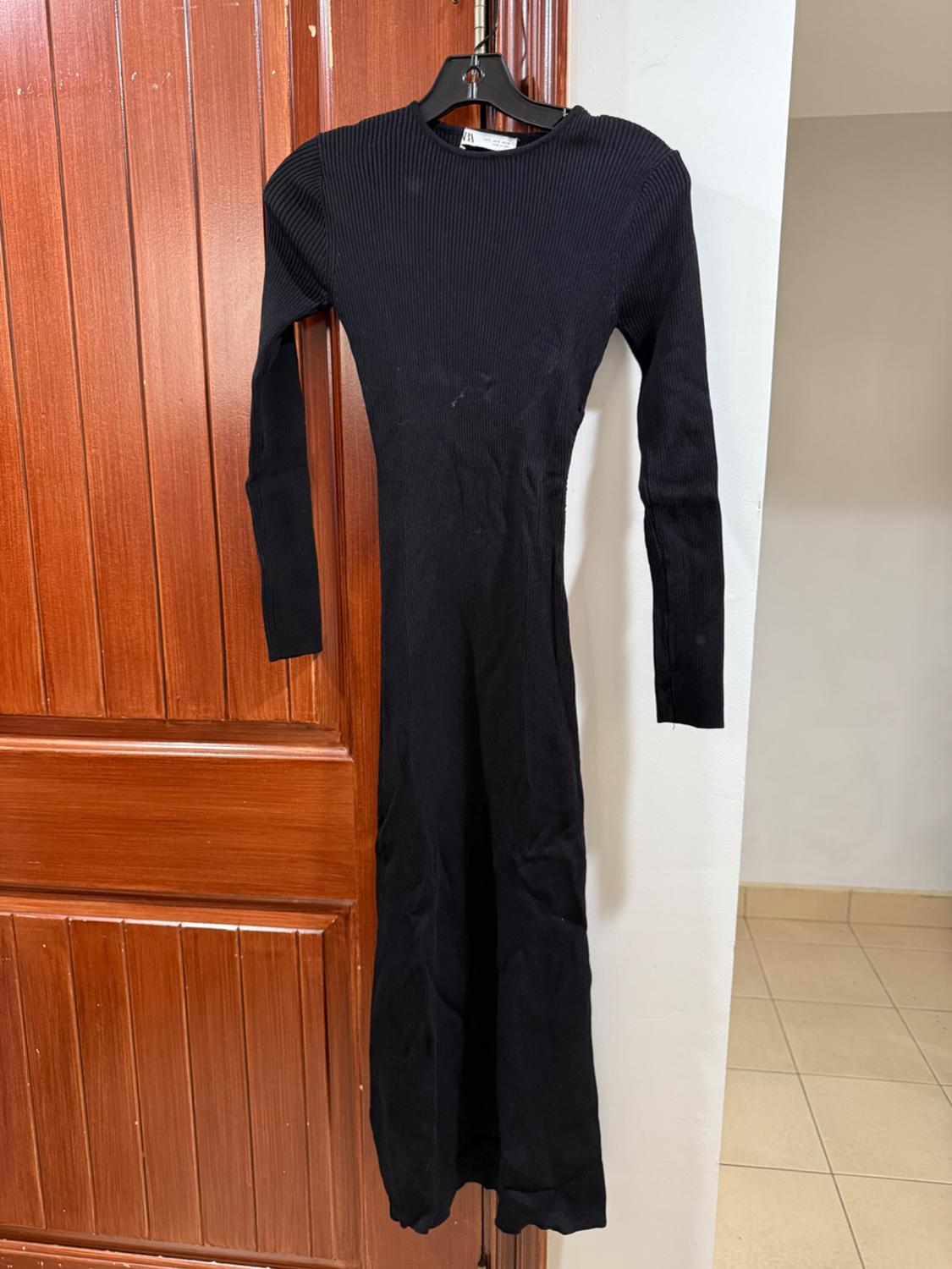 Long-sleeved black dress hanging on a wooden door. The dress is form-fitting and has a ribbed design.