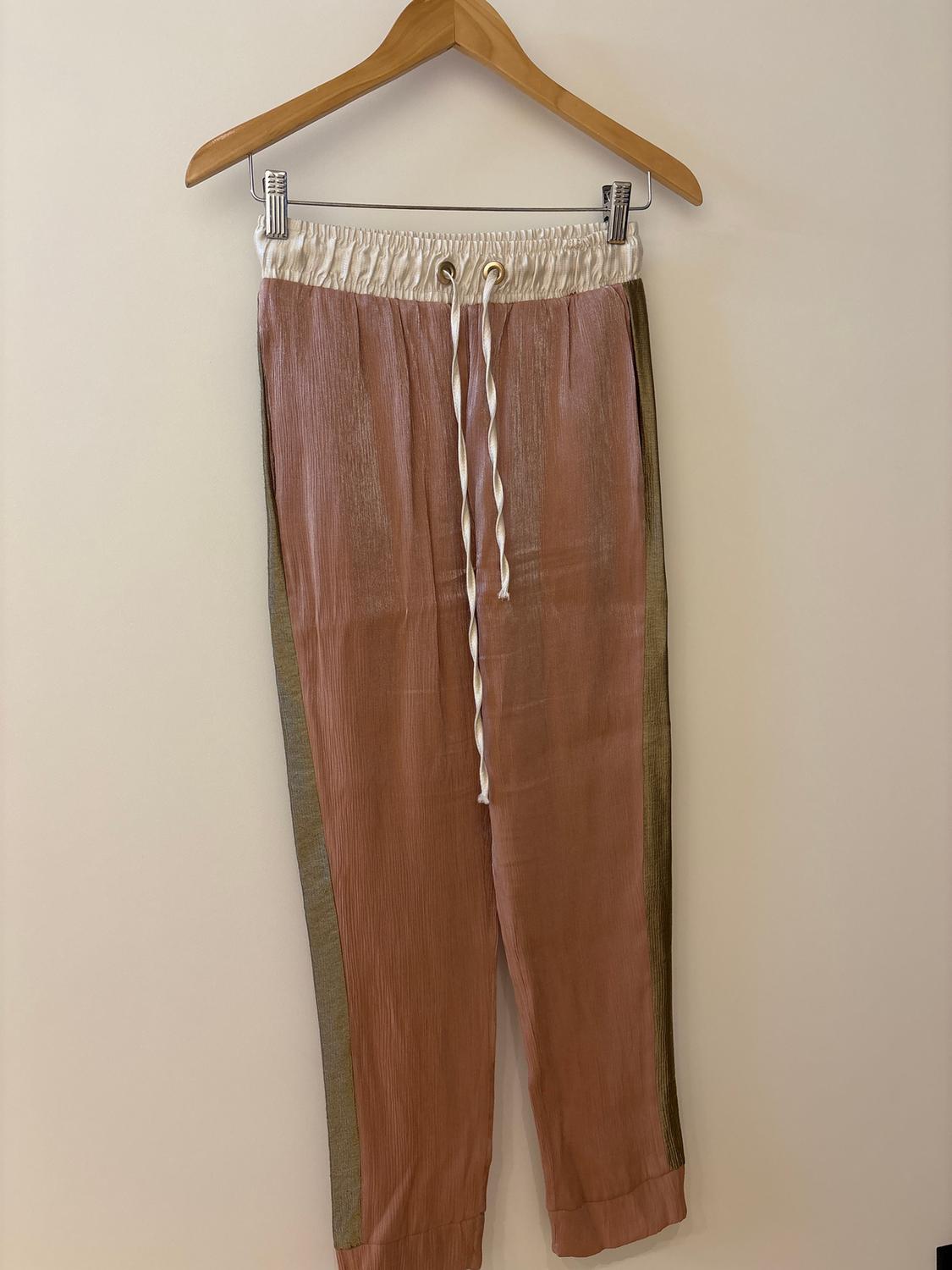 Trousers hanging on a wooden hanger, pink with a white elasticated waistband and drawstrings, olive green side details.