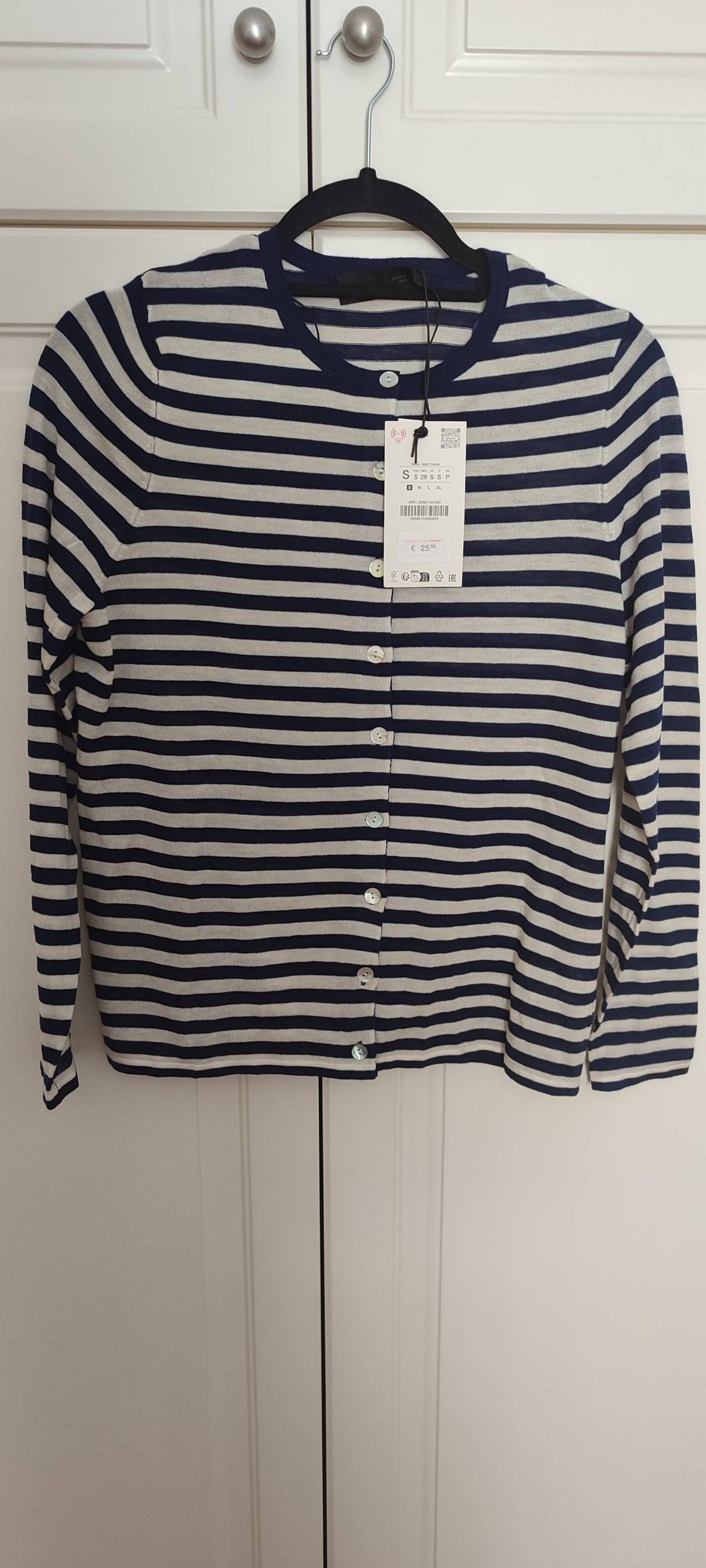 Navy and white striped cardigan hanging on a black hanger. Visible tag with price of €25.