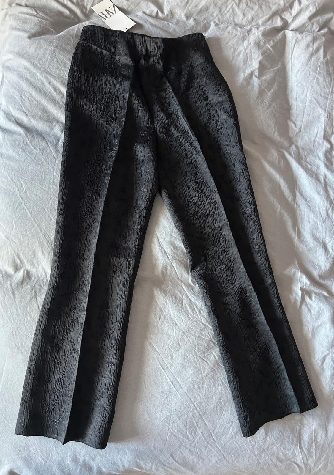 Black textured trousers on a light surface. Label visible in the top left.