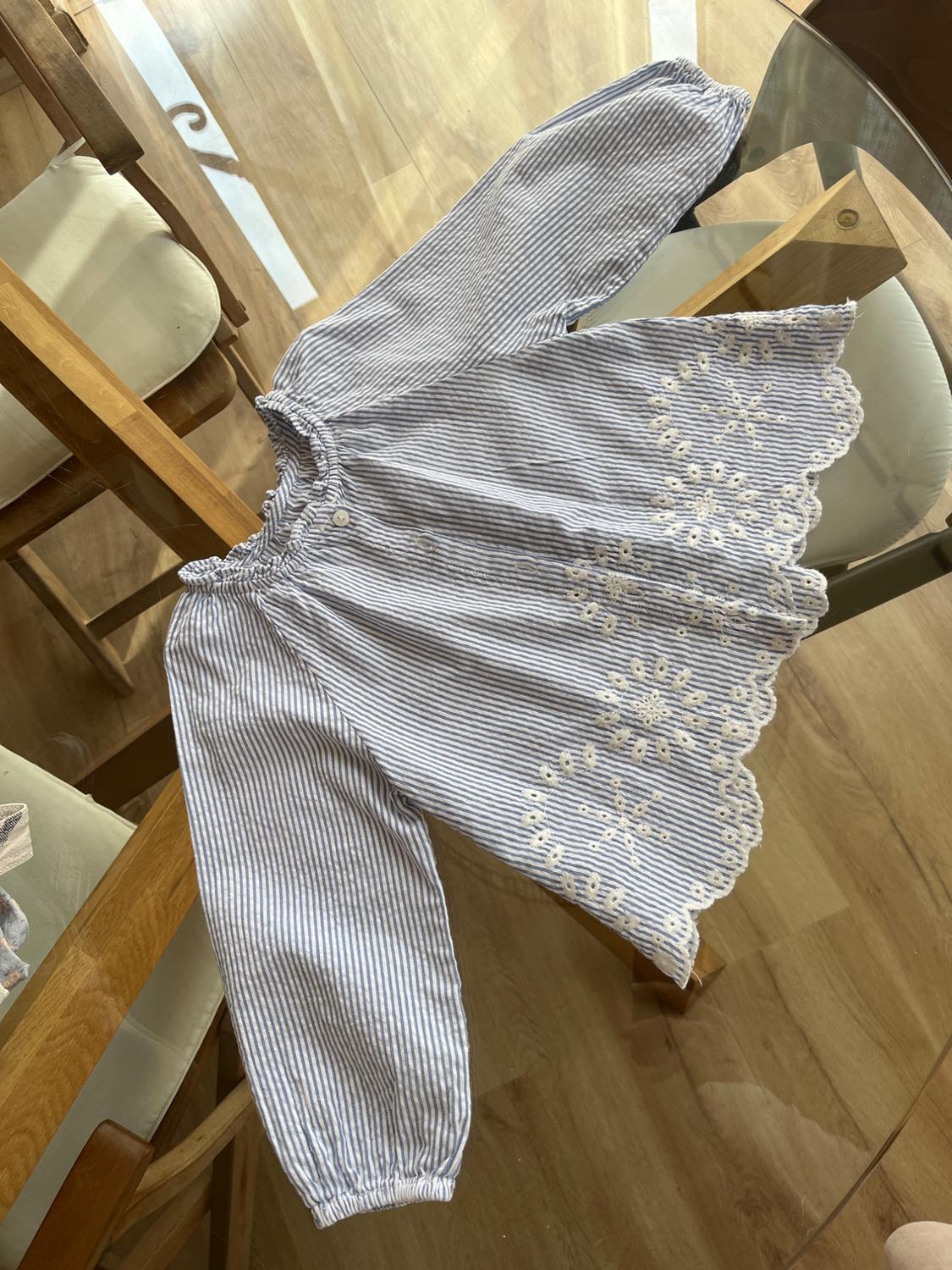 Blue and white striped blouse with floral embroidery on the hem, on a glass table with wooden chairs around it.