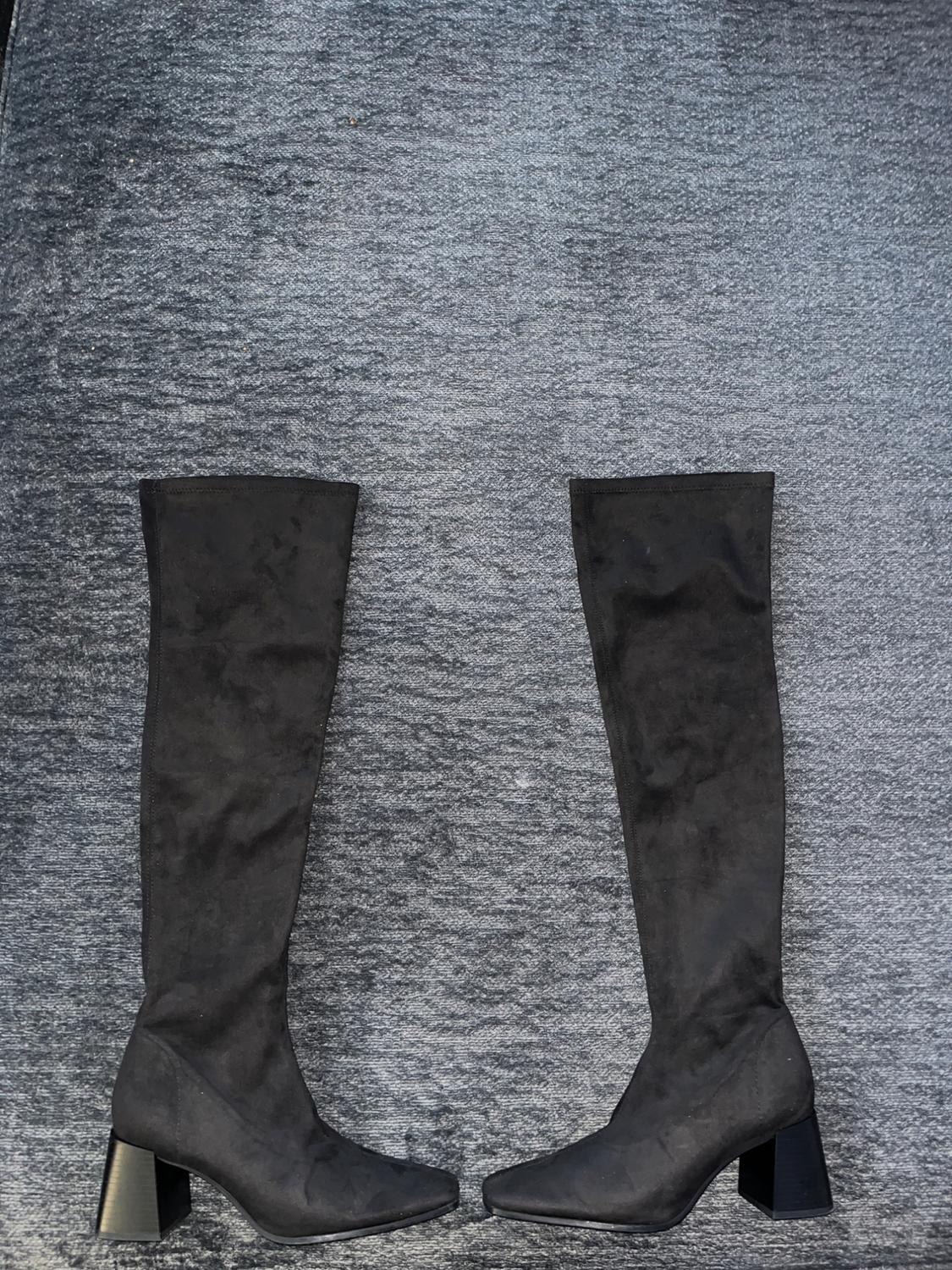 Black, high-heeled, square-heeled boots on a grey carpet. They are standing upright, facing each other.