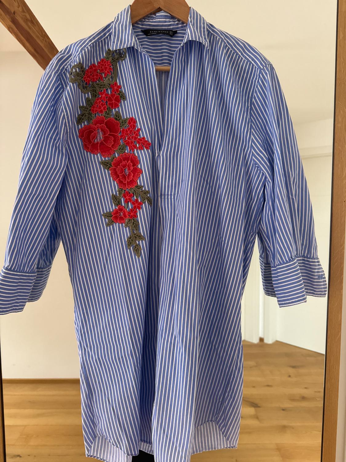 Front view of a blue striped shirt with red floral embroidery on the chest.