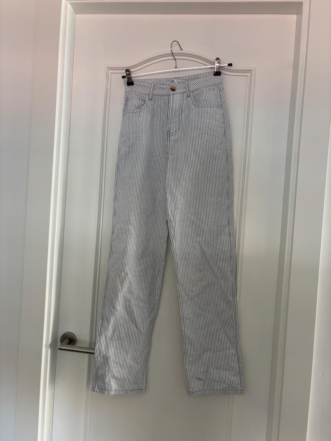 White and blue vertically striped trousers hanging on a white door with a metal coat hanger.