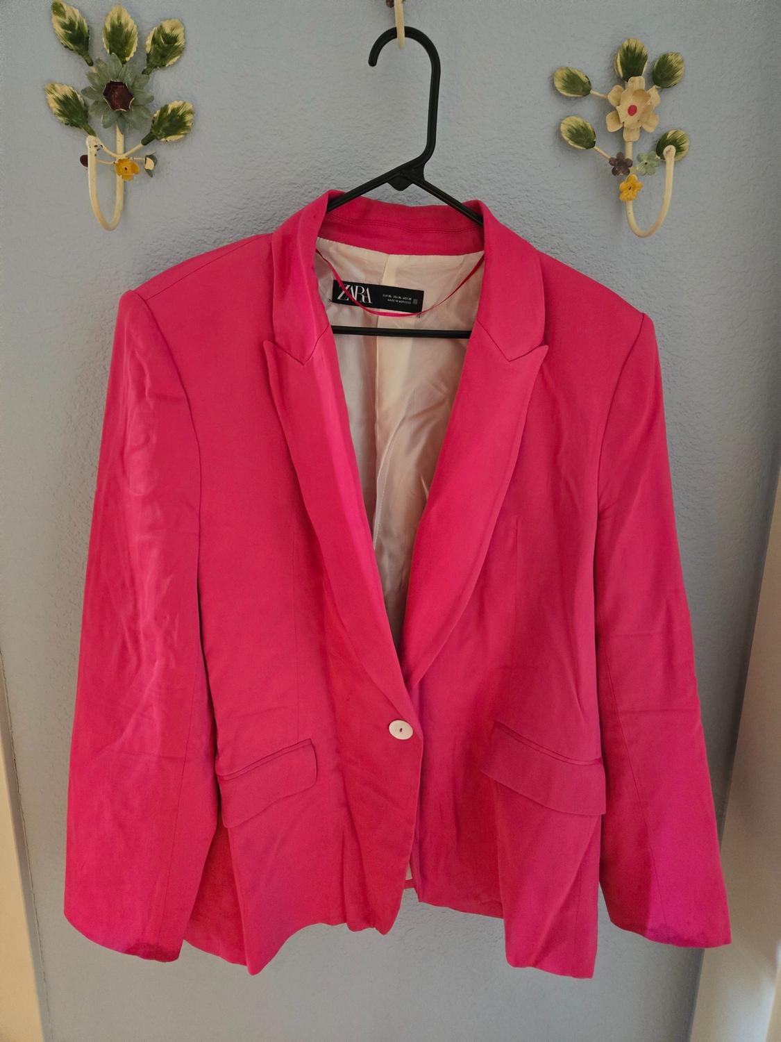 Bright pink jacket hanging on a black hanger against a light blue wall, with decorative floral details around it.