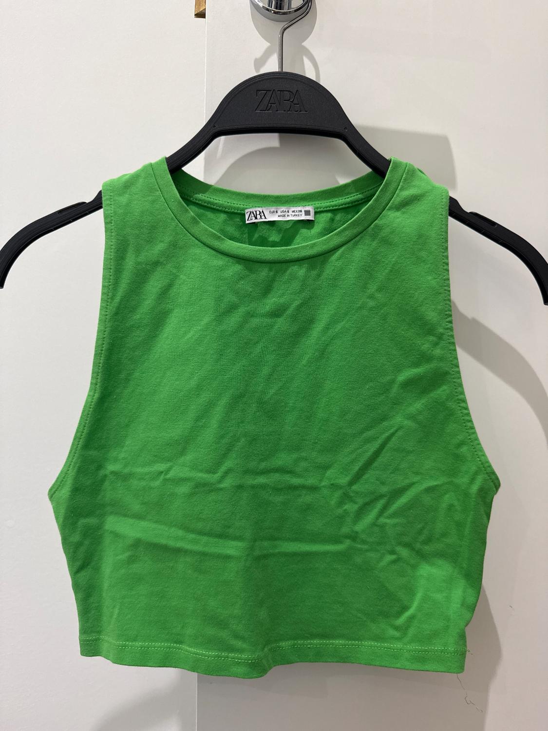 Green crop top hanging on a black hanger with visible branding. Plain white background.