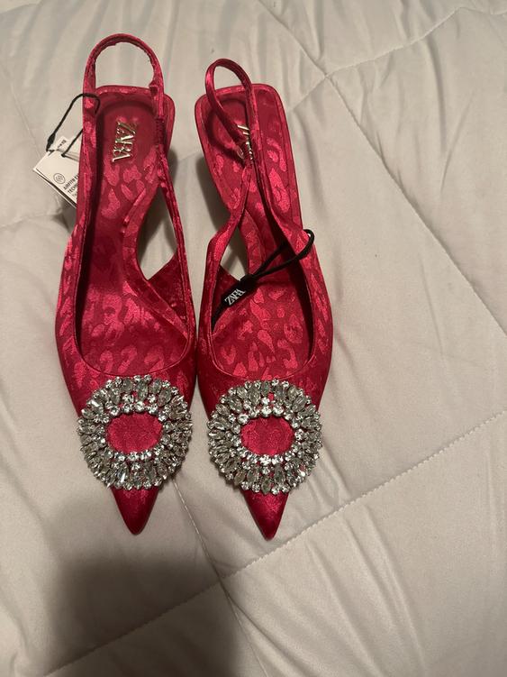 Red high heels with a floral print and a rhinestone brooch on the toe. Visible tag with the Zara logo.