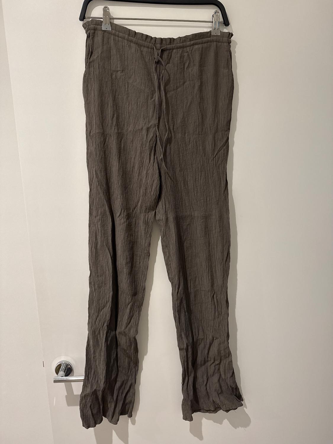 Dark brown crinkled fabric trousers hanging on a black hanger against a white wall.