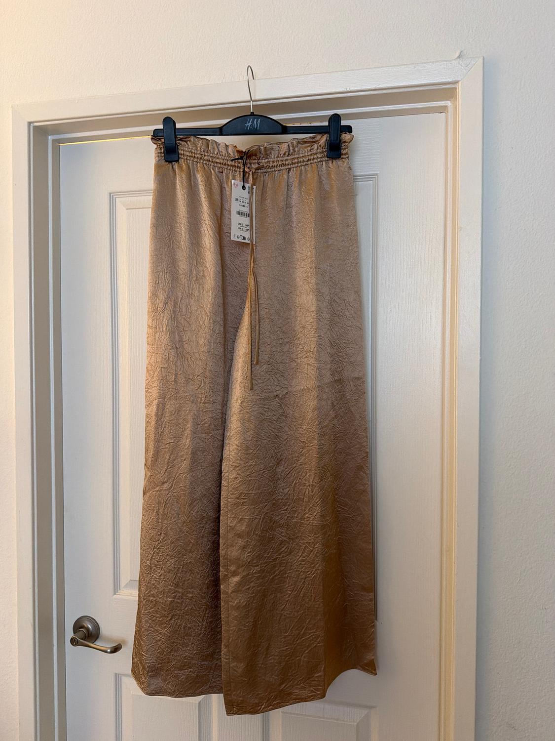 Gold pants hanging on a black hanger with a visible tag, over a white door with a silver doorknob.