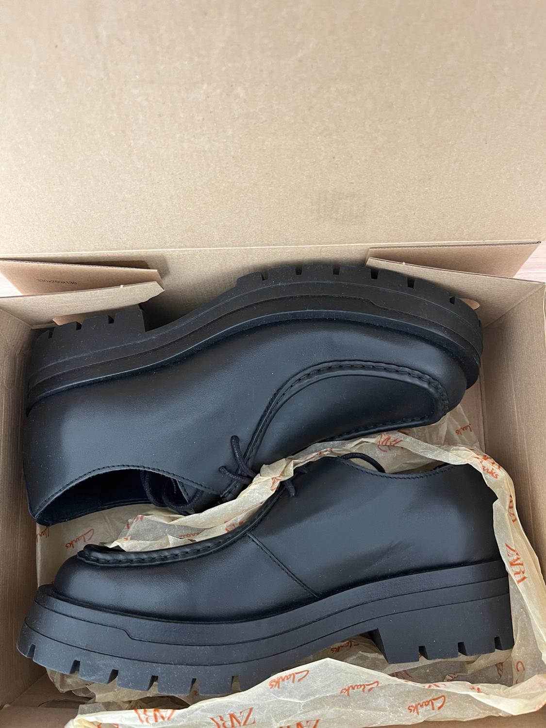 Black lace-up shoes with a thick sole in a cardboard box on tissue paper with the text Zara, Clarks and 330x250x130.