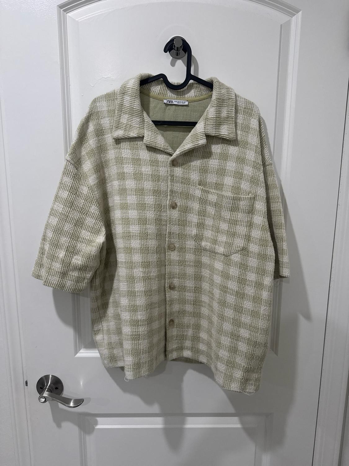 Textured short-sleeve shirt in light green and white plaid, hanging on a hanger over a white door. Tag with the text ZARA.