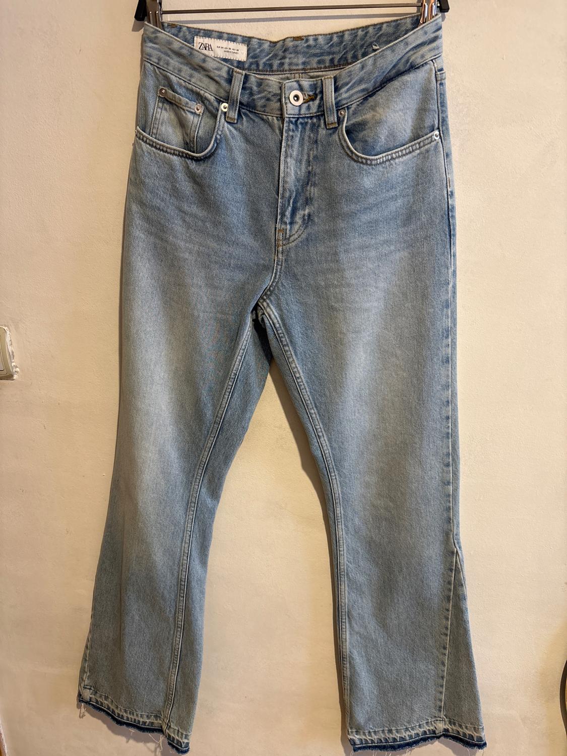 Light blue jeans hanging on a hanger, with a visible label on the waist. Beige background.