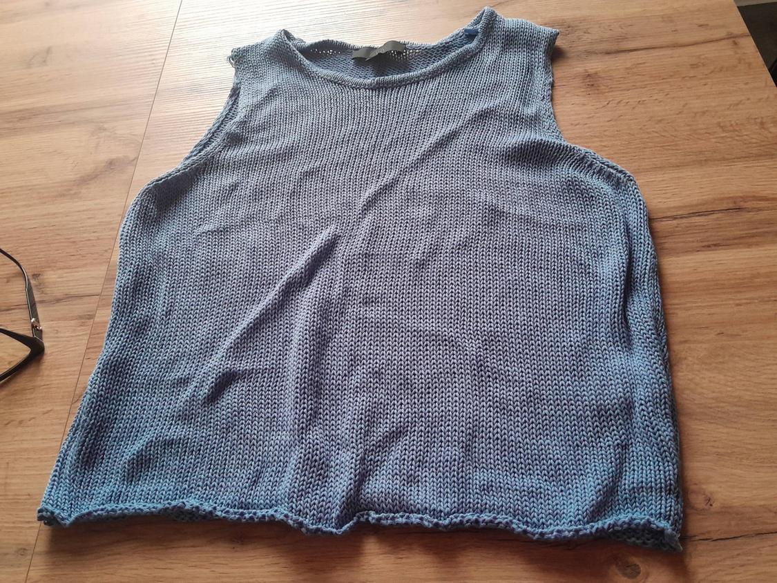 Blue knitted vest top on a wooden table. To the left, a pair of black glasses can be seen.