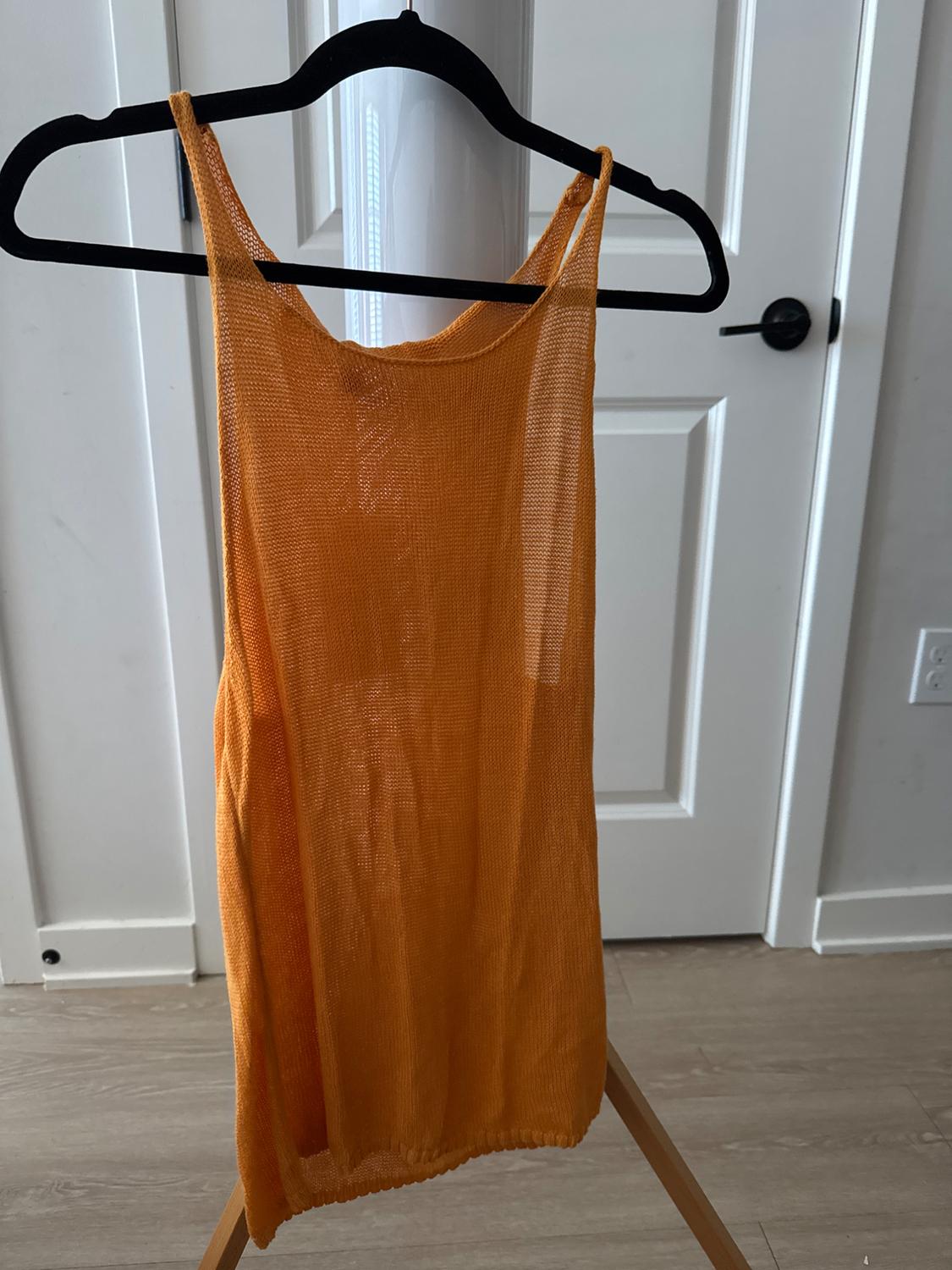 Sleeveless orange dress hanging on a black coat hanger, in front of a white door on a light wood floor.