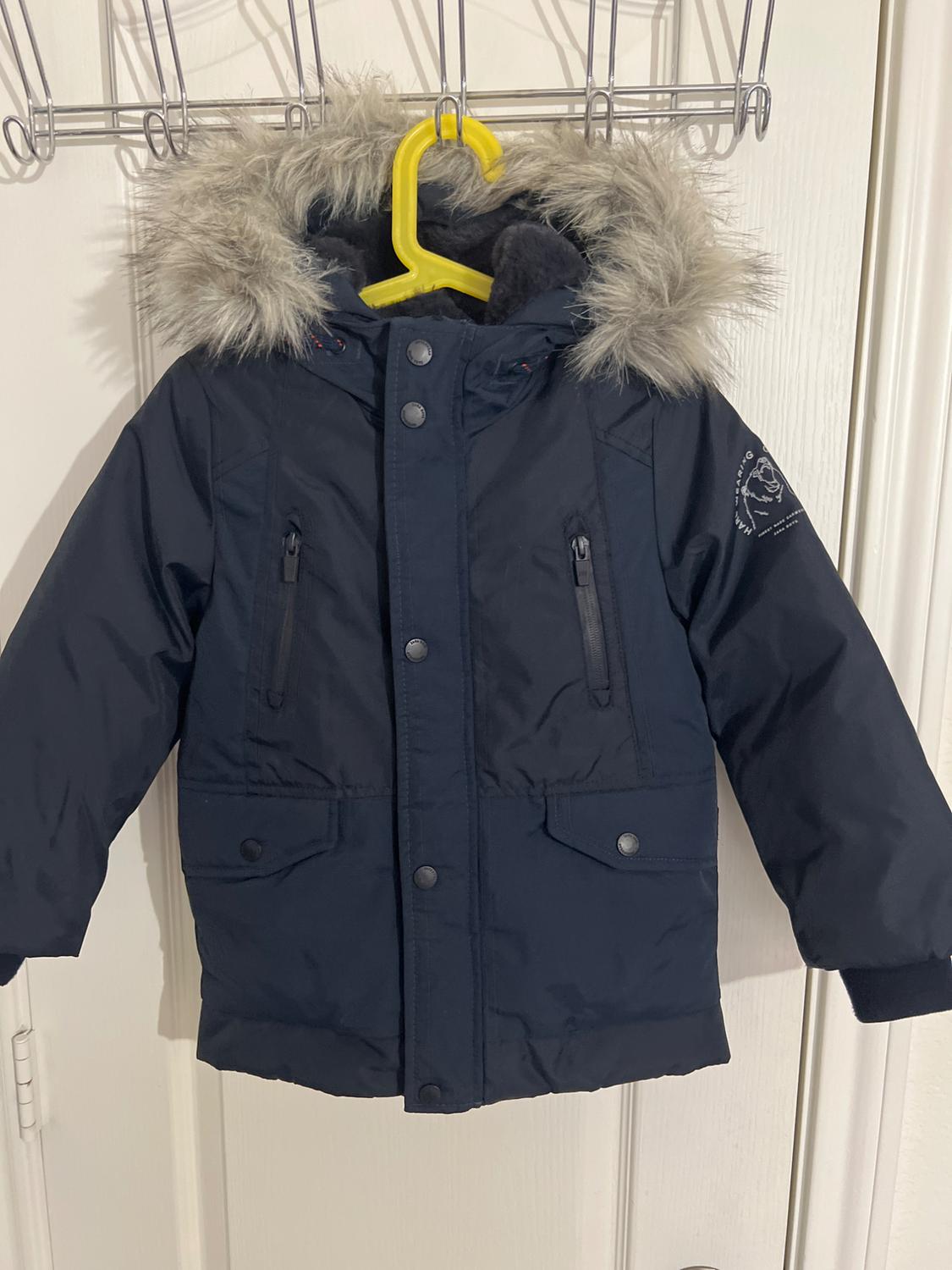 Navy blue jacket with a fur hood and pockets, hanging on a yellow hanger over a white door.
