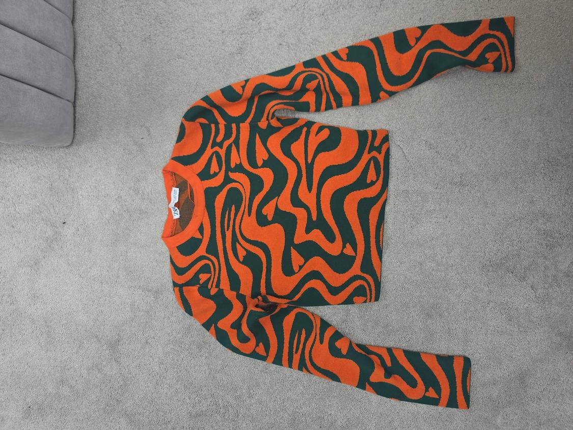 Long-sleeved jumper with a wavy orange and green print on a grey background. Visible label on the collar.