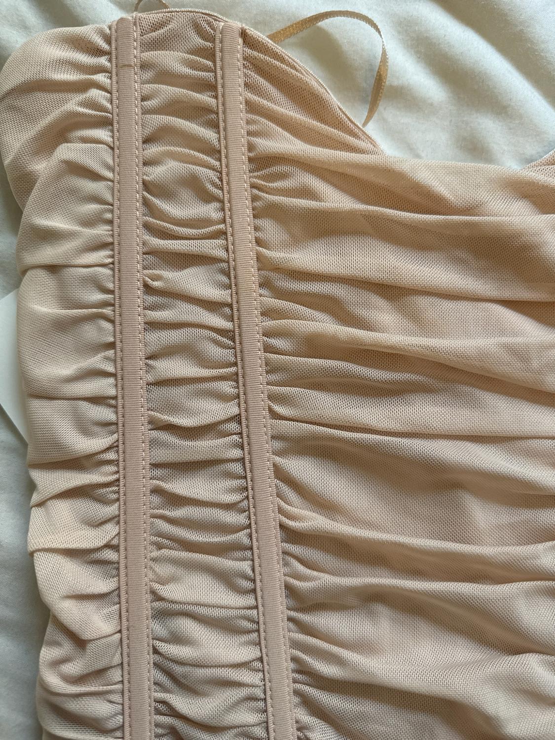 Close-up of a light beige garment with gathered tulle fabric and vertical seams, on a white fabric surface.