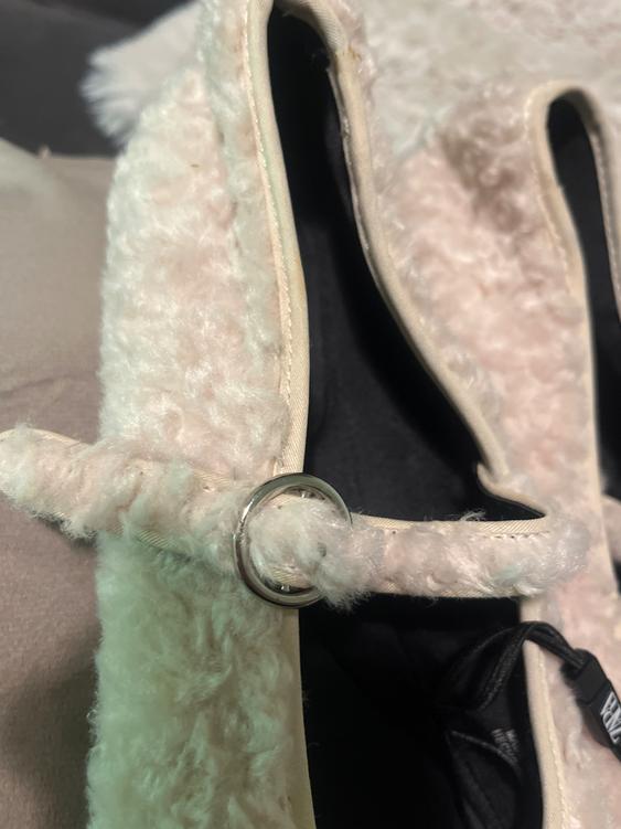 Detail of a white fluffy fabric garment with a metal ring. Dark background and partially visible label.