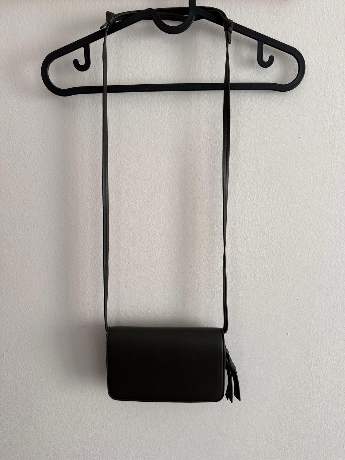 Black handbag hanging on a black hook against a white wall. Minimalist and elegant design with a long, adjustable strap.