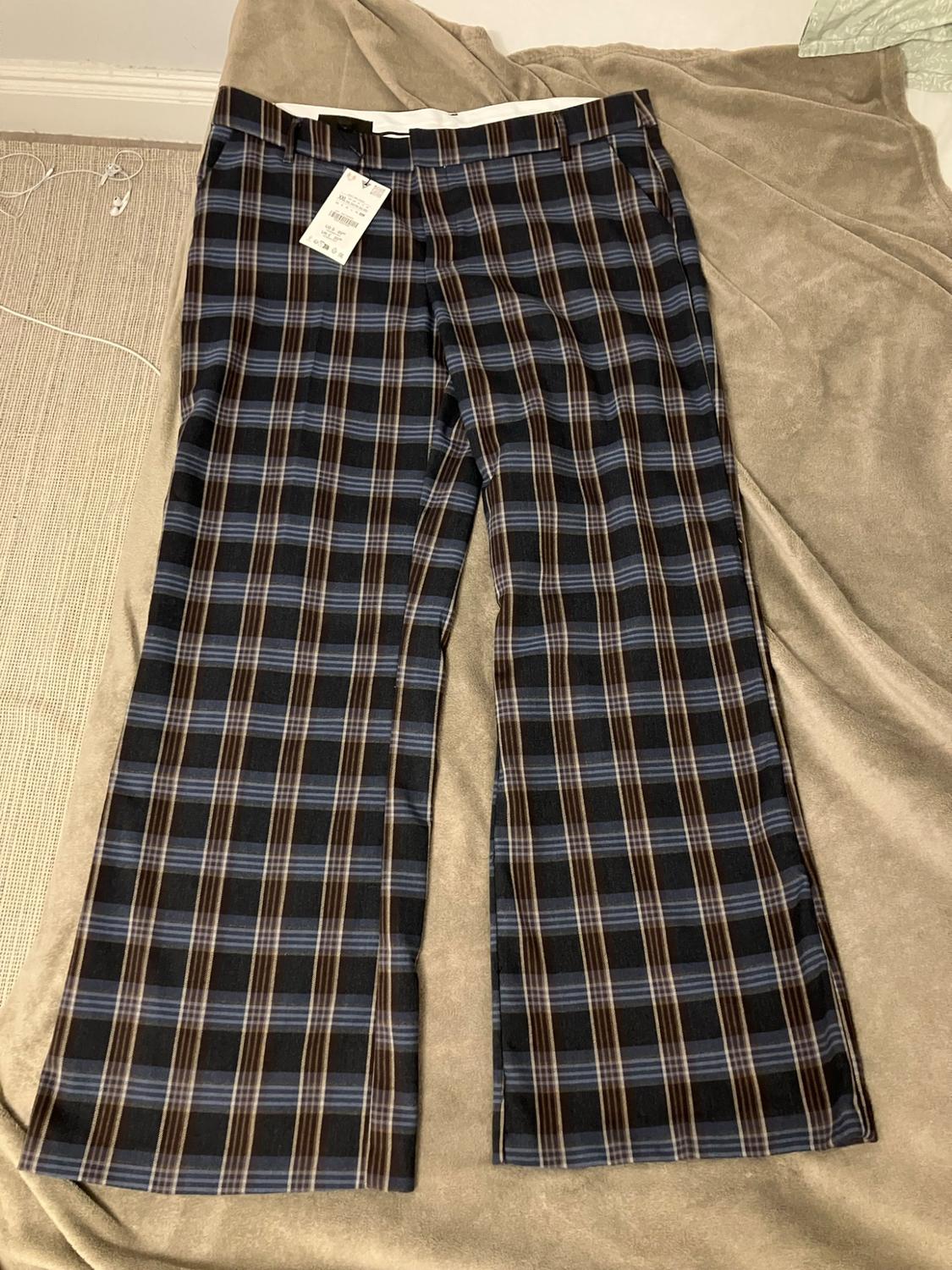 Blue and brown checked trousers with tag, on a beige blanket in a relaxed setting.