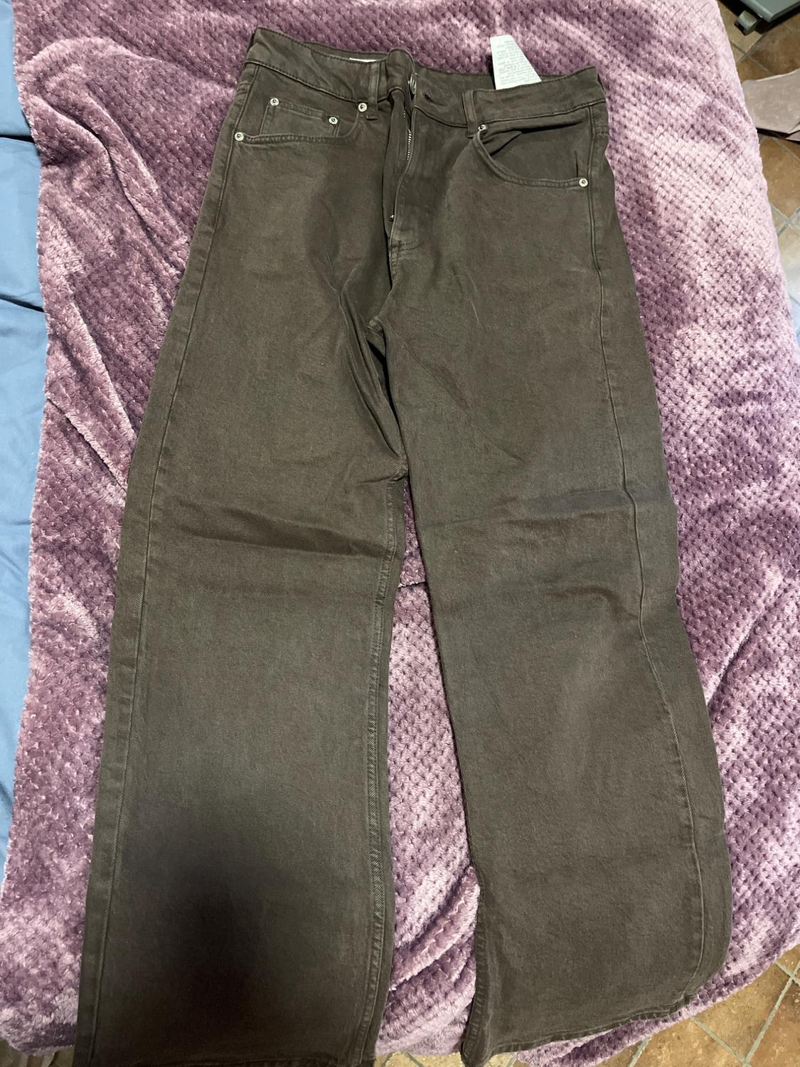 Brown, straight-cut trousers on a textured purple blanket. A white label is visible on the back pocket.