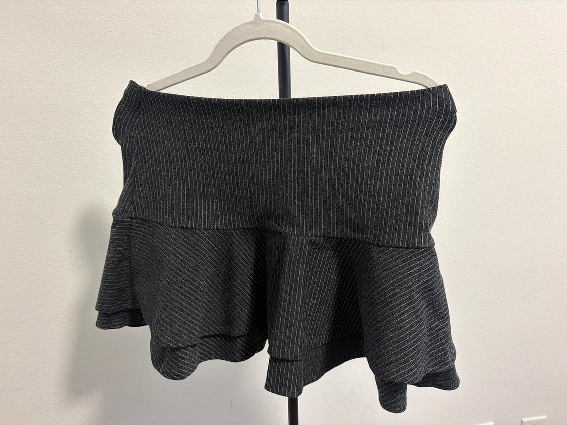 Gray short skirt with ruffles and vertical stripes, hanging on a white hanger against a white background.